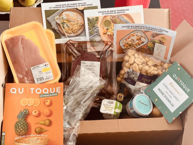 Screenshot 2025-03-28 at 6.30.14 PM Contenu d’une box repas Quitoque avec recettes imprimées, viande fraîche, gnocchis, condiments, légumes et le magazine Quitoque.
