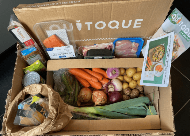 Screenshot 2025-03-28 at 6.50.08 PM Contenu d’une box repas Quitoque avec légumes frais (carottes, poireaux, oignons, pommes de terre), viandes, poisson, produits secs, recettes imprimées et le magazine Quitoque.