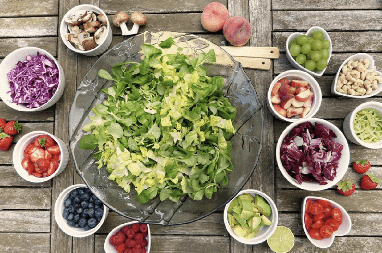 Screenshot 2025-03-31 at 11.55.42 AM Grande assiette de salade verte entourée d’ingrédients frais et colorés comme des fruits rouges, légumes, noix et crudités