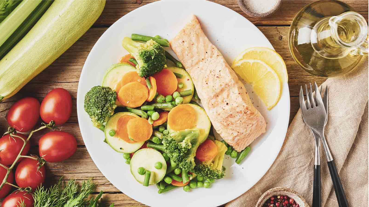 Screenshot 2025-04-27 at 11.10.53 AM Assiette saine composée d'un filet de saumon grillé, de légumes vapeur variés (brocoli, carottes, courgettes, petits pois) et de tranches de citron, sur une table en bois rustique
