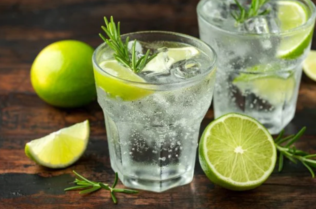 Screenshot 2025-06-13 at 2.04.52 PM Verres d’eau tonique fraîche avec glaçons, quartiers de citron vert et brins de romarin, sur une table en bois avec des citrons verts frais