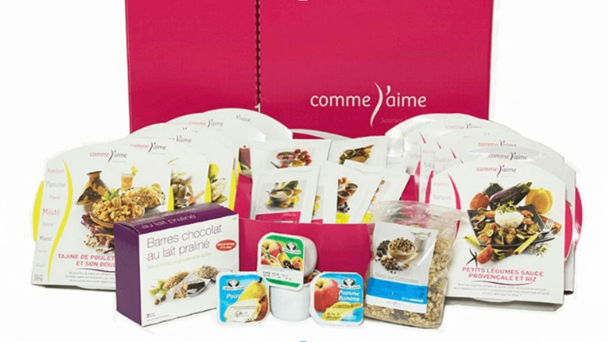 Screenshot 2025-07-06 at 12.43.34 PM Coffret minceur Comme J’aime avec repas prêts à consommer : plats cuisinés variés (tajine de poulet, petits légumes sauce provençale), barres chocolat au lait praliné, compotes, céréales muesli et encas, devant une boîte rose Comme J’aime