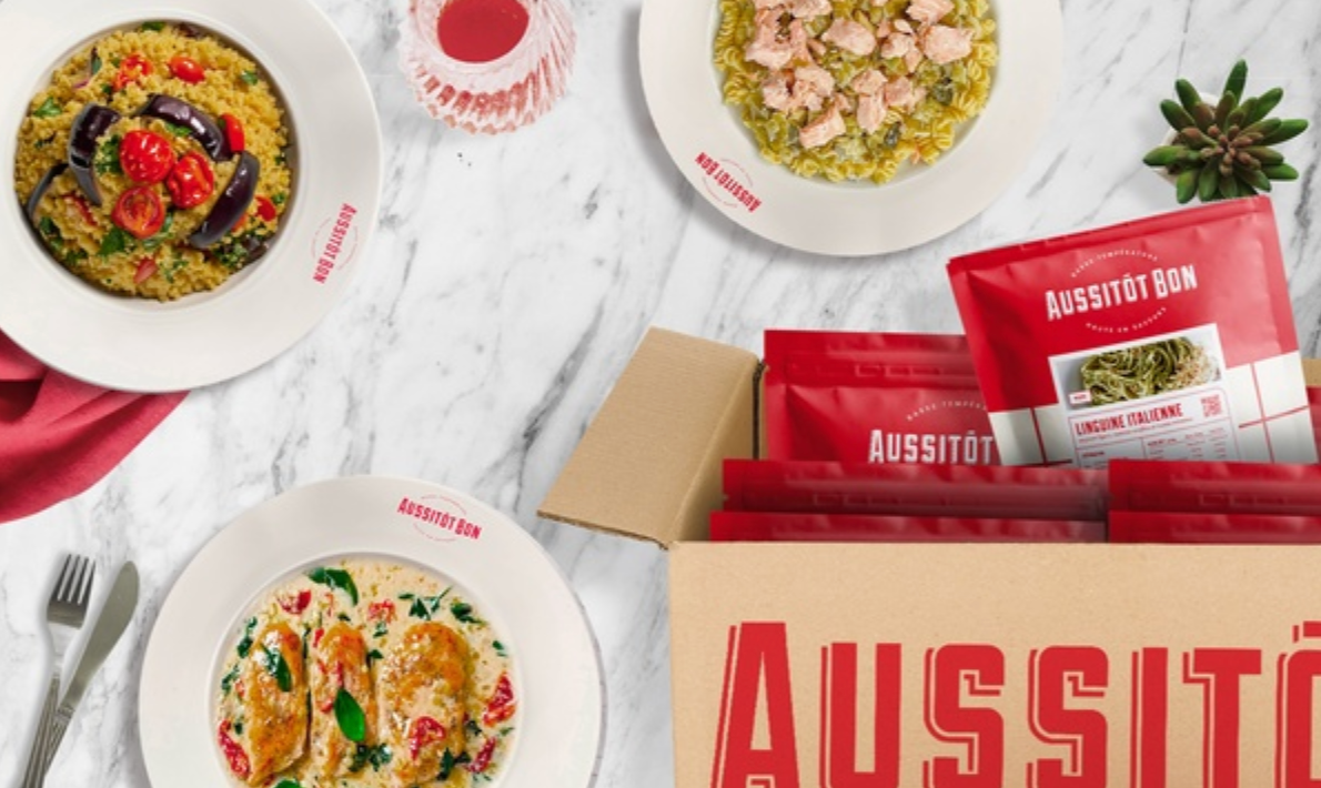 Screenshot 2025-07-26 at 10.37.23 AM Repas cuisinés Aussitôt Bon servis dans des assiettes et présentés avec leur packaging rouge dans un colis de livraison, prêts à réchauffer.