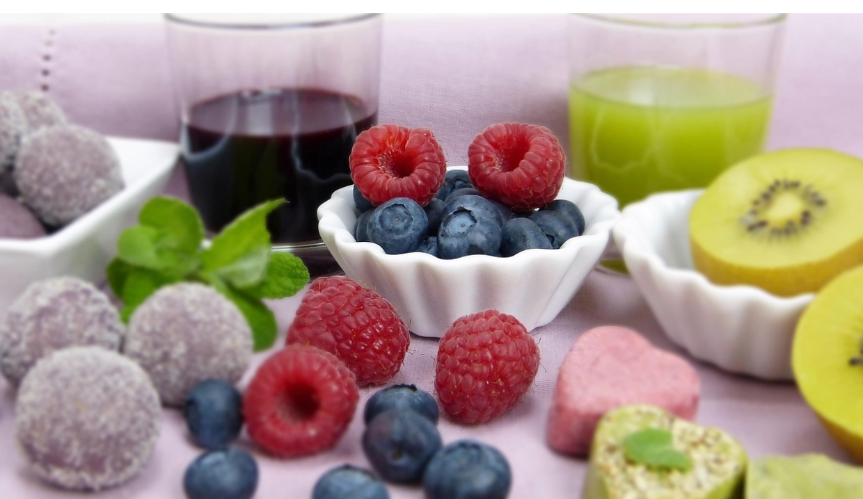 Assiette de fruits et gourmandises : framboises et myrtilles fraîches dans un ramequin blanc, truffes chocolatées enrobées de sucre, tranches de kiwi, boissons vertes et violettes, décorées de feuilles de menthe.