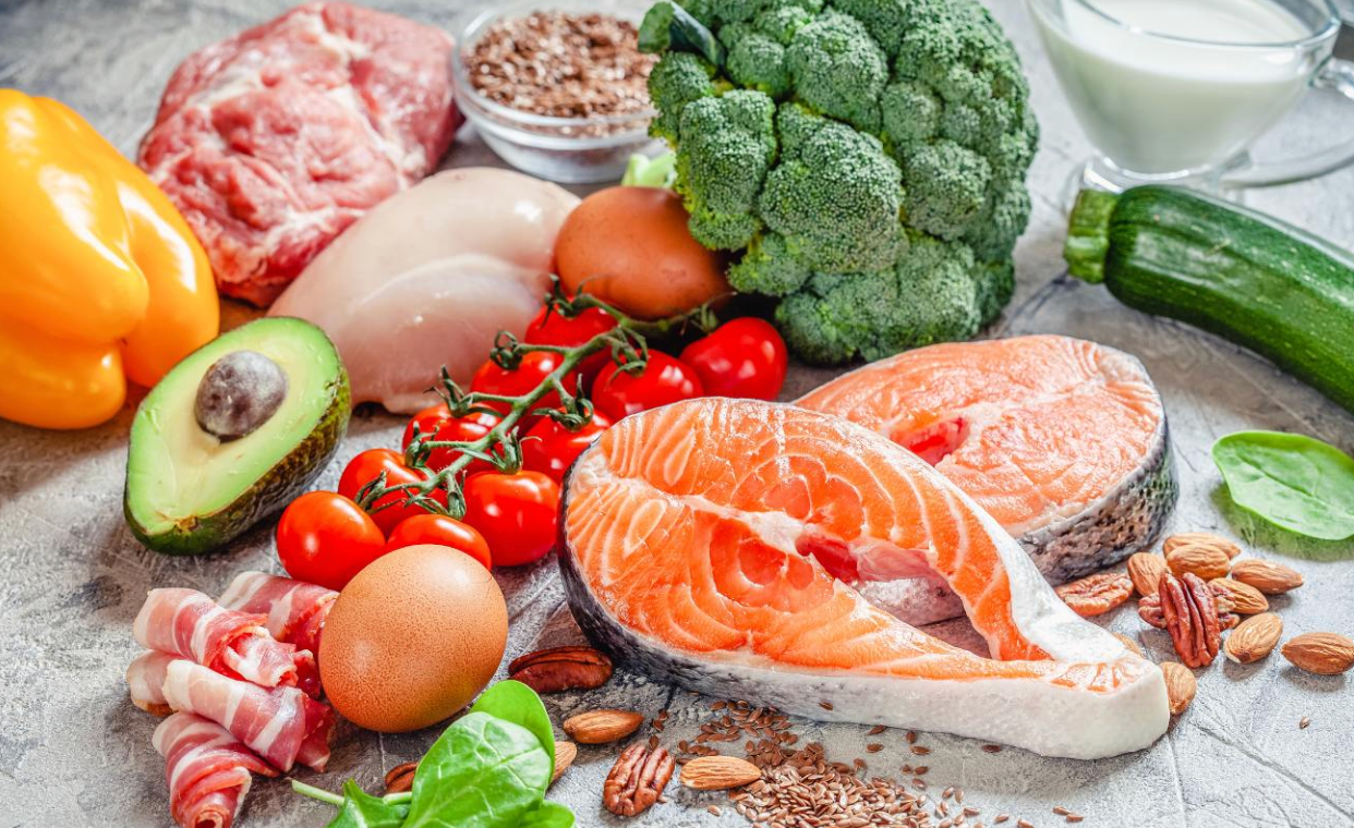 Assortiment d’aliments frais et sains : saumon, poulet, bœuf, œufs, avocat, brocoli, courgette, poivron jaune, tomates cerises, noix et verre de lait sur un plan de travail