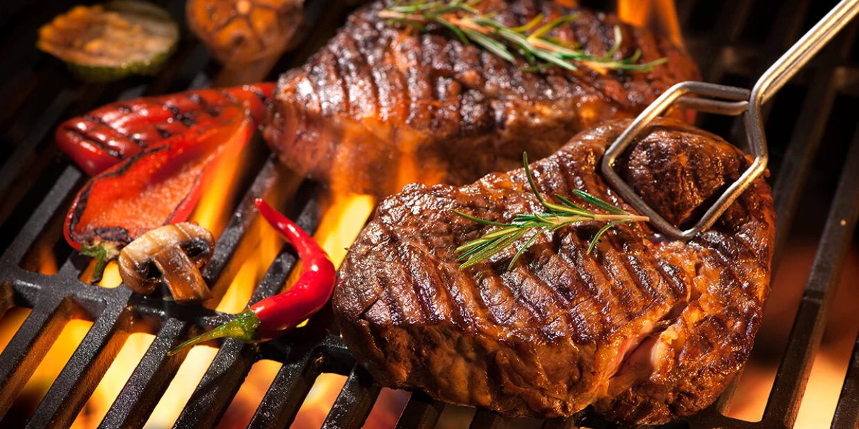 Steaks grillés au barbecue avec branches de romarin, poivrons, champignon et piment rouge sur les flammes