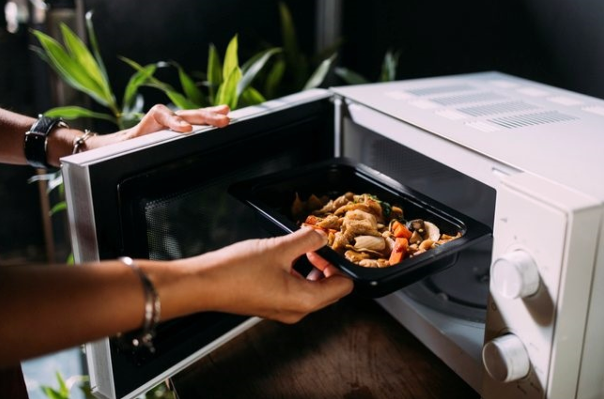Personne plaçant un plat de nourriture dans un four à micro-ondes pour le réchauffer