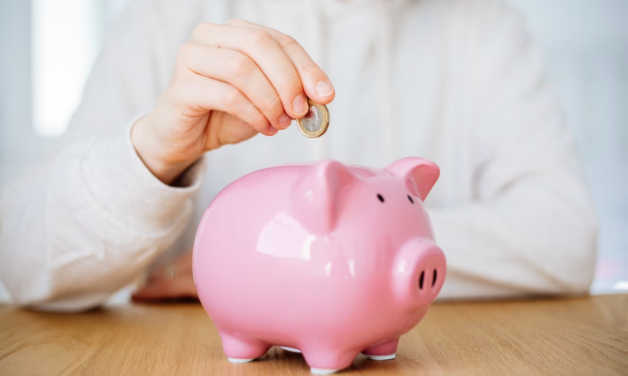 Personne déposant une pièce dans une tirelire rose en forme de cochon